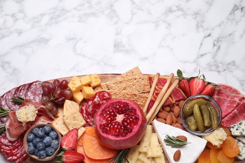 Preview: Wooden plate with different delicious snacks on white marble table, top view. Space for text