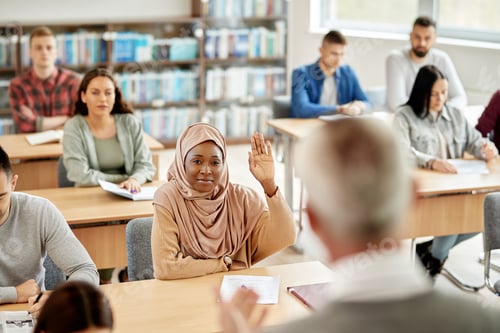 Preview: Black Muslim student raising her hand to answer teacher's question during a class in the classroom.