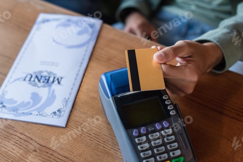 Preview: partial view of man with credit card near payment terminal and menu brochure on table