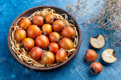 Preview: Front view of whole and chopped mespilus germanica inside and outside a brown bowl on blue