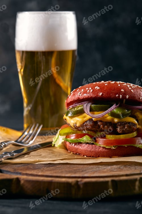 Preview: Juicy hamburger served with a glass of cold lager beer over an old wooden table with a dark