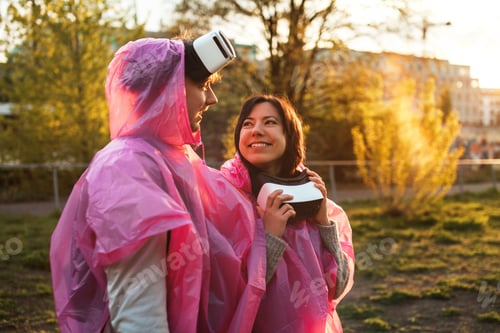 Preview: Closeup shot of a male and a female smiling in pink plastic raincoats and VR headsets taken off
