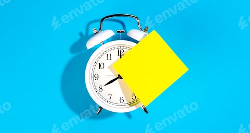 Preview: White alarm clock and blank yellow paper sticker on a blue background isolated.