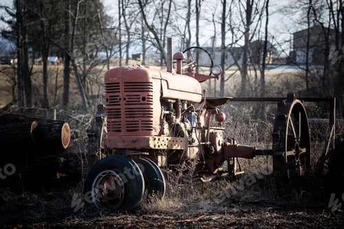 Preview: Closeup of an old red tractor parked in a field near the farm under sun