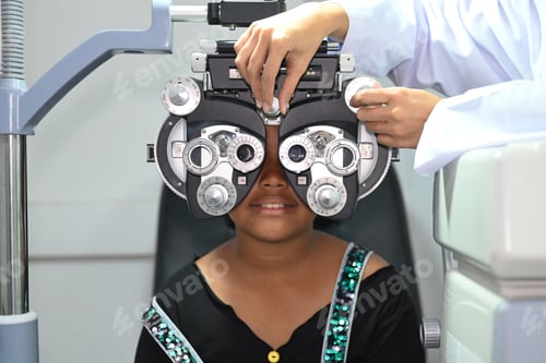 Preview: Smiling little girl testing vision or sight with optical phoropter in modern ophthalmology clinic.