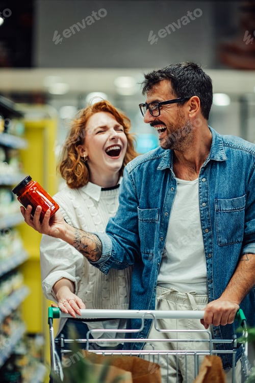 Preview: Cheerful couple laughing while grocery shopping in supermarket