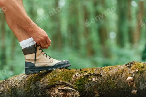 Preview: Ties shoelaces. Close up view of tourist that is in summer forest