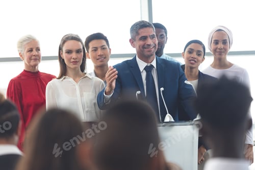 Preview: Businessman standing at podium with diverse colleagues and speaks at business seminar in office