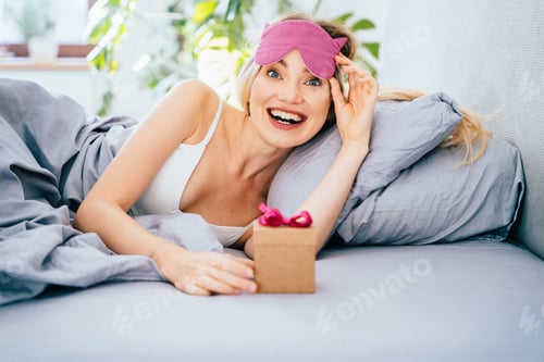 Preview: Woman Excitedly Holding Gift Box in Bed