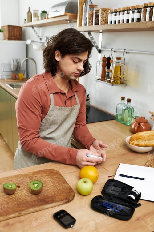 Preview: Young man manages diabetes in a modern kitchen while preparing healthy snacks
