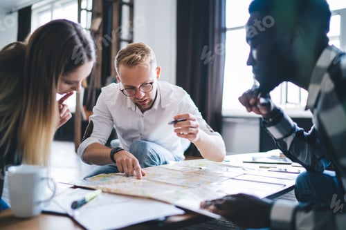Preview: Concentrated man working with diverse colleagues studying map in room