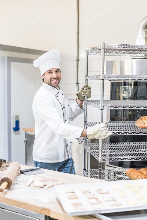 Preview: smiling male baker in chefs uniform standing at kitchen