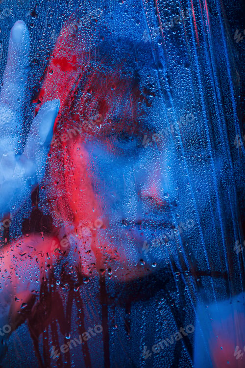 Preview: Studio shot in dark studio with neon light. Portrait of beautiful girl behind wet glass