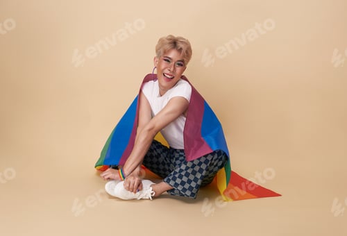 Preview: Youth asian transgender LGBT with Rainbow flag on shoulder isolated over nude color background.