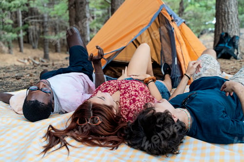 Preview: Diverse group of young friends relaxing and talking together on a blanket at a campsite