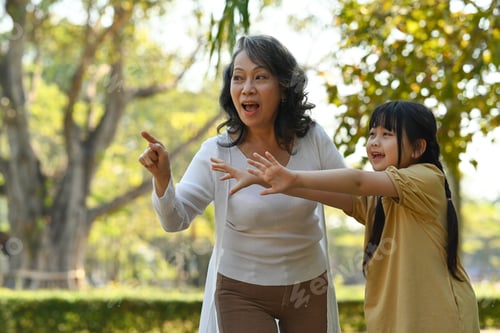 Preview: Joyful little asian child having fun while walking in public park with grandmother.