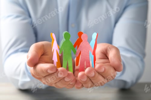 Preview: Man holding paper human figures at table, closeup. Diversity and inclusion concept