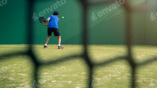 Preview: Padel player with black racket playing a match in the open behind the net court