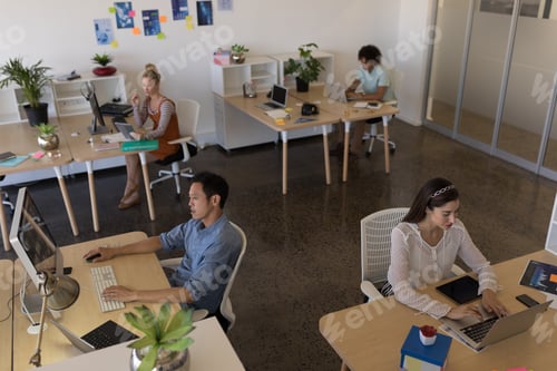 Preview: High angle view of diverse business people working at individual desks in modern office