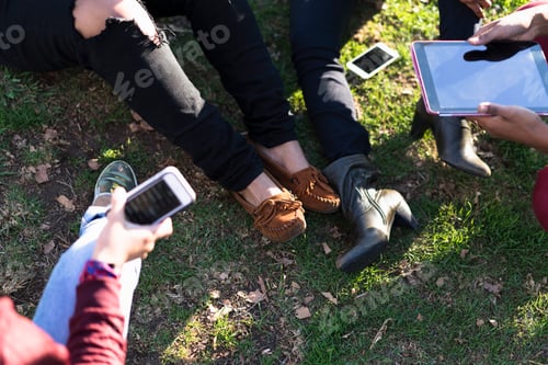 Preview: Group of female friends relaxing in park, using digital tablet and smartphone, low section