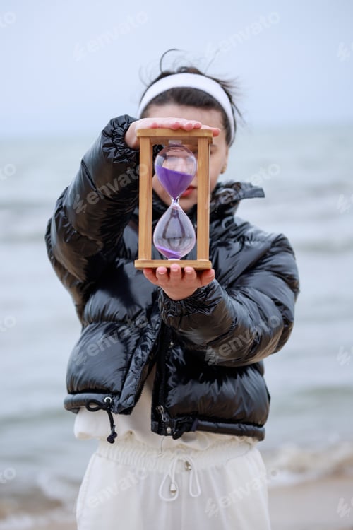 Preview: Young female holding sand clock at the beach
