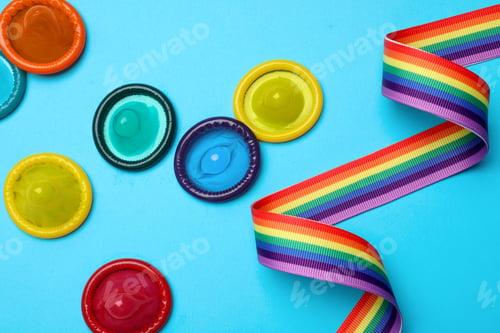 Preview: Colorful condoms and rainbow ribbon on light blue background, flat lay. LGBT concept