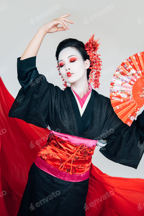 Preview: beautiful geisha in black kimono with hand fan dancing near red cloth on background isolated on