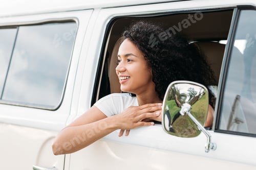 Preview: Smiling mixed race woman looks out from van window enjoying a road trip