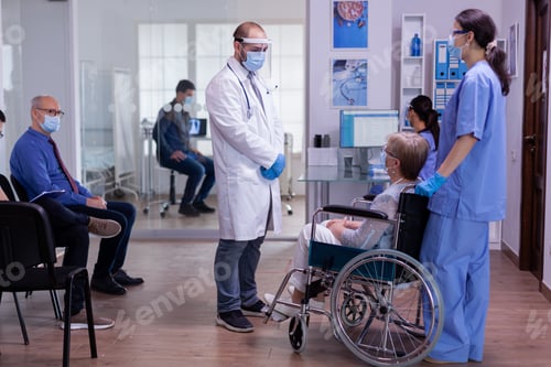 Preview: Medical staff with protection mask talking with disabled woman