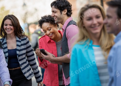 Preview: A group of men and women in the city, two looking at a cell phone screen and laughing.