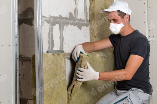 Preview: Worker in protective respirator mask insulating rock wool insulation in wooden frame