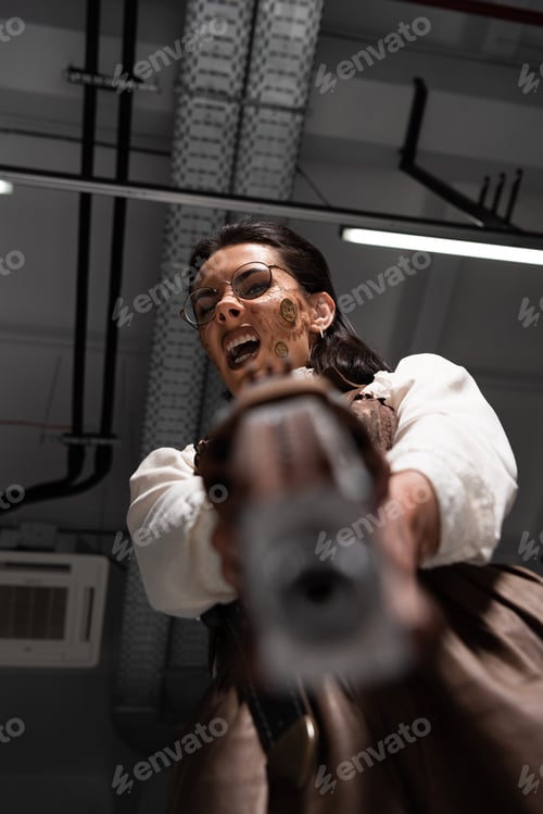 Preview: selective focus of angry steampunk woman screaming and aiming with pistol at camera