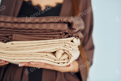 Preview: Close up view of young woman that standing against wall with bed clothes in hands