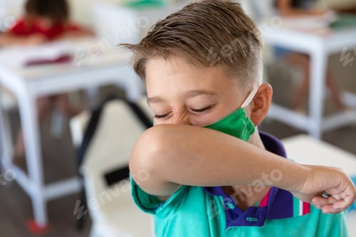 Preview: Boy wearing face mask sneezing while covering his mouth at school