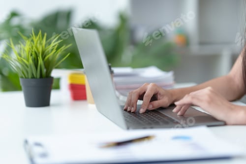Preview: Close-up of the hands of a business woman attentively typing on a laptop computer and having a docum