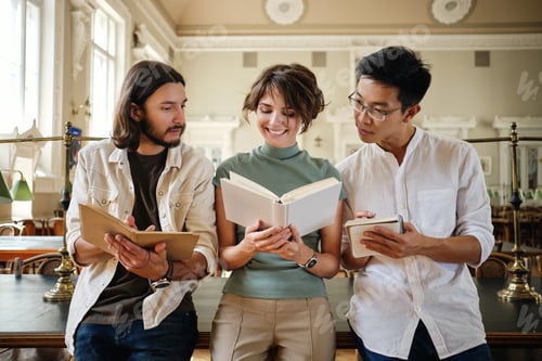 Preview: Group of young multinational students happily studying with book together in library of university