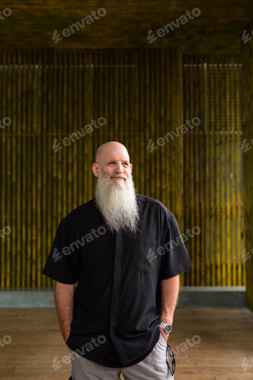 Preview: Portrait of man bald man with long gray beard outdoors against bamboo wall thinking