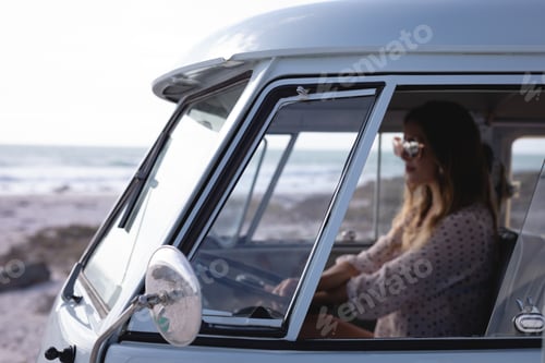 Preview: Side view of beautiful Caucasian woman driving camper van at beach on a sunny day