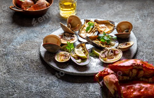 Preview: Raw seafood, crabs, clams and mussels shellfish with lemon and cilantro on gray plate.