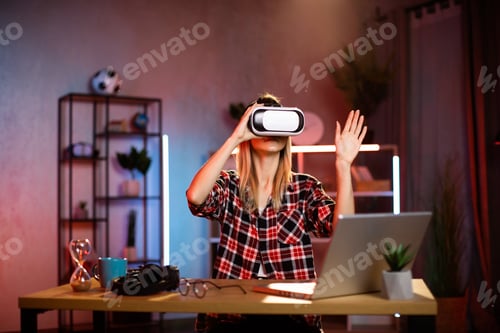 Preview: Young cheerful woman in VR goggles working in augmented reality while staying at home.