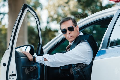 Preview: selective focus of mature policeman in bulletproof vest and sunglasses walking out from car