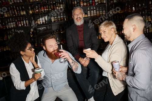 Preview: cheerful bearded man looking at camera near multiethnic colleagues drinking cocktails in bar