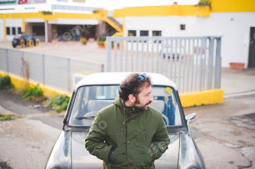 Preview: Mid adult man leaning on vintage car looking over his shoulder