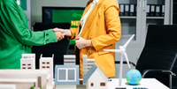 Preview: Businesswomen shaking hands in a green office with renewable energy models, net zero and