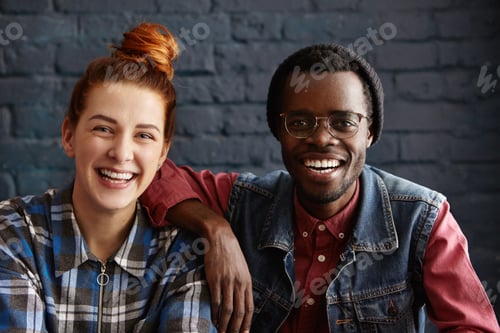 Preview: Attractive African American male in hat and glasses resting arm on shoulder of beautiful young redhe