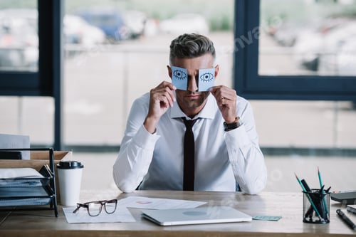 Preview: businessman holding sticky notes with drawn eyes near face