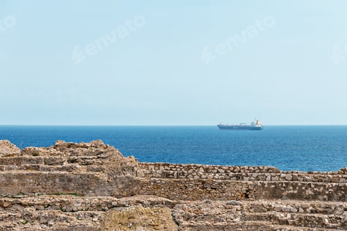 Preview: ruins of an ancient amphitheater and a cargo ship sailing in the mediterranean sea