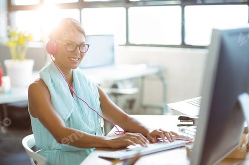 Preview: Woman typing on keyboard at modern office desk, wearing pink headphones and glasses