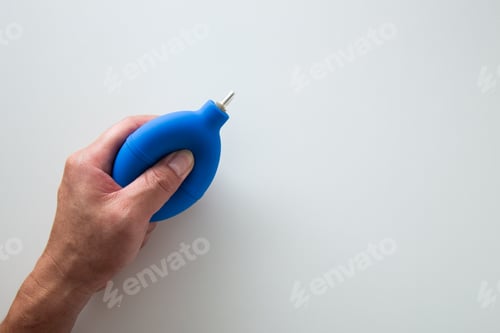 Preview: Hand is squeezing a blue air blower pump dust cleaner on a white background