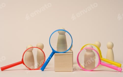 Preview: Wooden figures of men stand on a beige background and a plastic magnifying glass.